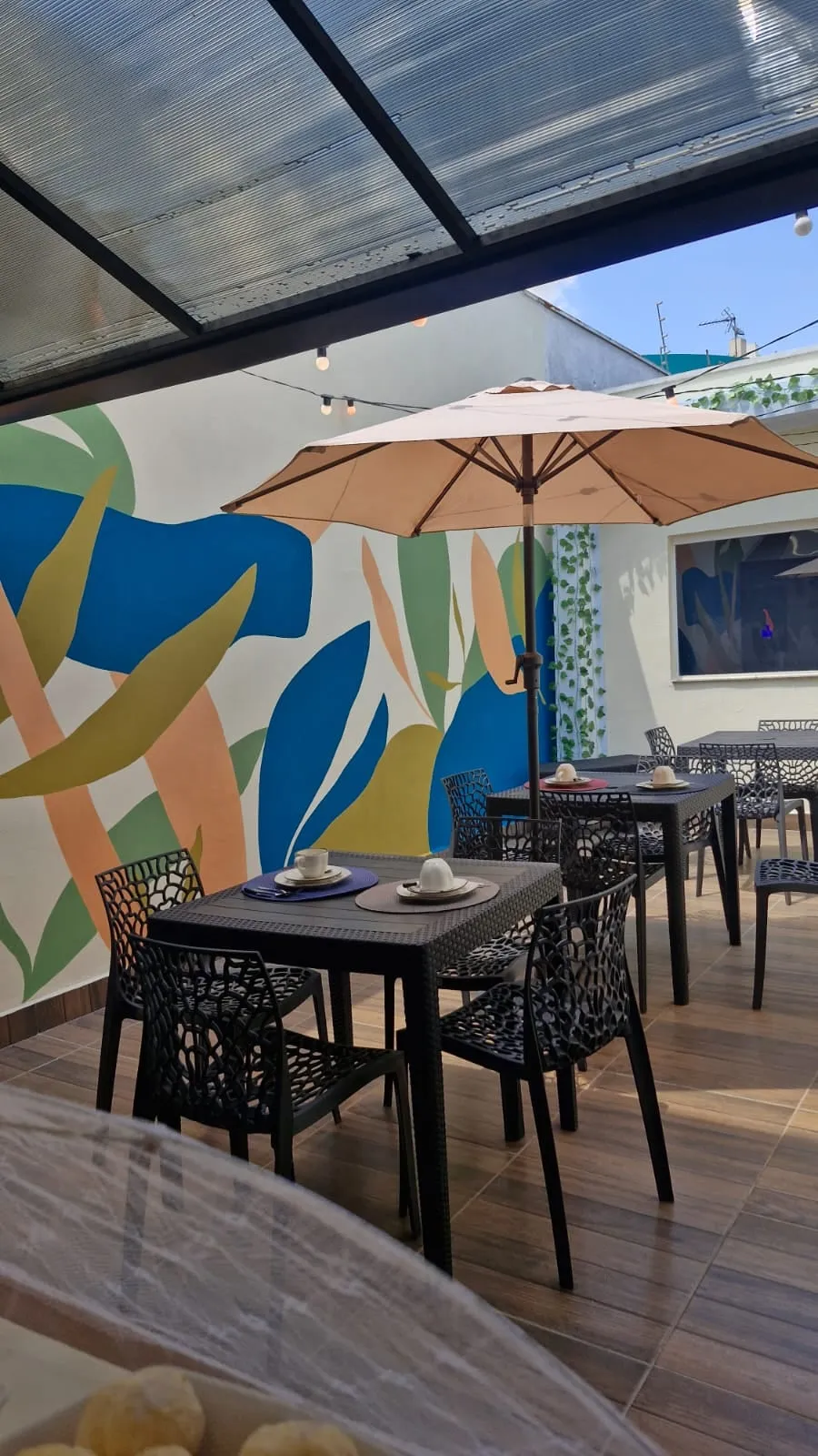 Área de convivência com mesas, guarda-sol e mural colorido